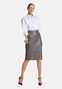 Grijze leren kokerrok met stiksels aan de voorkant, gecombineerd met een witte blouse met knopen. Model draagt bordeauxrode hoge hakken.
