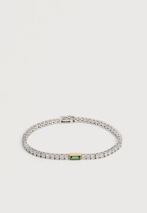 Bracelet de tennis en argent avec des pierres claires rondes et une unique pierre précieuse verte rectangulaire sertie en or au centre, sur fond blanc.