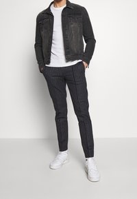 Czarna kurtka dżinsowa na białym, gładkim t-shircie, zestawiona z granatowymi spodniami w paski i białymi trampkami. Strój ma casualowy charakter.