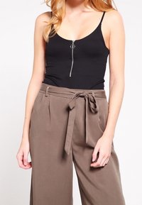 Zwart geribd tanktopje met een voorrits en spaghetti bandjes, gecombineerd met taupekleurige, wijde broek met hoge taille en een ceintuur die geknoopt is.