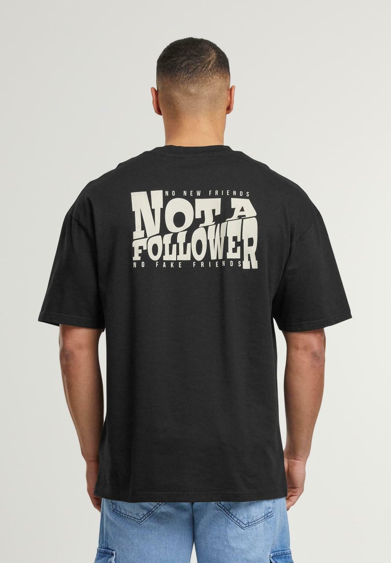 Zwart katoenen T-shirt met op de achterkant een grote witte opdruk "NOT A FOLLOWER", met extra tekst erboven en eronder.