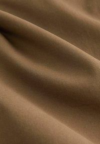 Pruun kangas, millel on sile tekstuur ja peen ribimustriga, rippumas, et näidata selle painduvat kuju ja pehmet läiget.