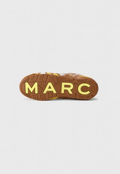 Brun sneakersål med gule "MARC" bogstaver, tekstureret gummi for greb og en karakteristisk mønster. Hvide detaljer synlige på siderne.