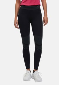 Rekbare zwarte leggings met een gestructureerde tailleband en met patronen versierde accenten op het onderste deel van de benen. Gepaard met witte sportschoenen.
