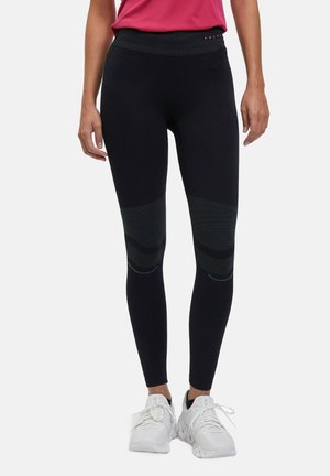 Dehnbare schwarze Leggings mit einem strukturierten Bund und gemusterten Akzenten am unteren Bein. Kombiniert mit weißen Sportschuhen.