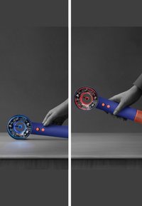 Hand som håller en blå och orange hårtork med synliga interna komponenter belysta av blått ljus på vänster sida och rött ljus på höger sida.