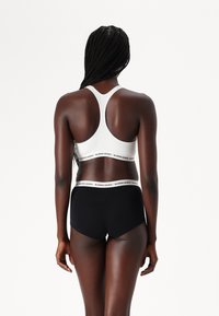 Sport BH i hvitt med svart logo-bånd; parret med svarte høyt i livet shorts med matchende logo-bånd. Glatt, elastisk stoff.