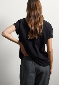 Top nero a maniche corte con risvolti, vestibilità morbida, abbinato a pantaloni grigi con tasche laterali e un tessuto texturizzato.