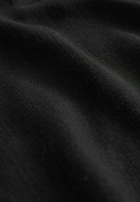 Mustaa kangasta, jolla on sileä pinta, esittäen hienovaraisia eroja kudoksessa ja pinnassa. Materiaali vaikuttaa kevyeltä ja hieman heijastavalta.