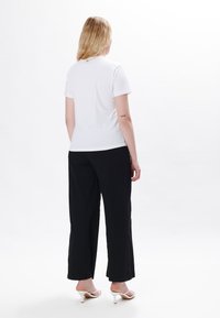 Hvid bomulds t-shirt med korte ærmer, parret med løse sorte bukser. Outfitet afsluttes med hvide højhælede sandaler.