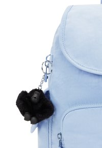 Zaino blu chiaro con chiusura a pattina, spalline regolabili e un portachiavi a forma di gorilla nero e peloso attaccato a un anello in argento.