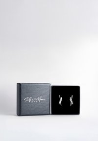 Silverörhängen i en svart sammetask. Örh ängena har en knutdesign med slanka, polerade metallkomponenter. Asken har en strukturerad, mörkblå utsida.