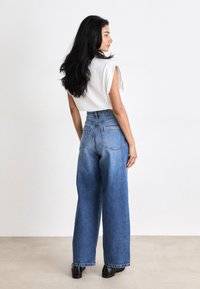Hoge taille, wijdvallende blauwe denim jeans met een lichte wassing, achterzakken en een rafelrand; gecombineerd met een simpel wit mouwloos topje.