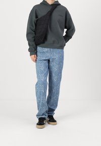 Sudadera verde oscura, pantalones azul claro con estampado de rosas, bolso cruzado negro y zapatillas negras con suela de goma. Look casual de moda urbana.