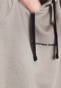 Light gray hoodie with a drawstring in black. Features "REDEFINED REBEL" printed in black, showcasing a soft fabric texture.