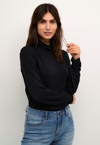 Juoda ilgomis rankovėmis turtleneck palaidinė, pagaminta iš minkštos medžiagos, pasižyminti laisvu kirpimu ir sukniubtomis apykaklėmis, derinama su šviesiai mėlynomis didelio juosmens džinsomis.