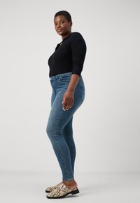 Black long-sleeve top paired with light blue skinny jeans. Footwear features a snake print design with a low heel.