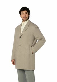 Beiger Wollmischmantel mit Reverskragen, zwei Knöpfen, Seitentaschen und strukturierter Oberfläche, kombiniert mit einem cremefarbenen Pullover und grauen Hosen.