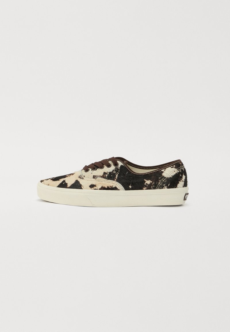 Canvas sneakers featuring a cowhide pattern in black and beige, brown laces, and a white rubber sole. Low-top design with rounded toe.