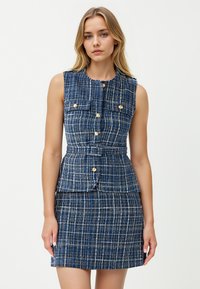 Abito senza maniche blu navy con un motivo a quadri testurizzato, caratterizzato da bottoni dorati e un accentuato punto vita a peplo. Include due tasche sul petto.