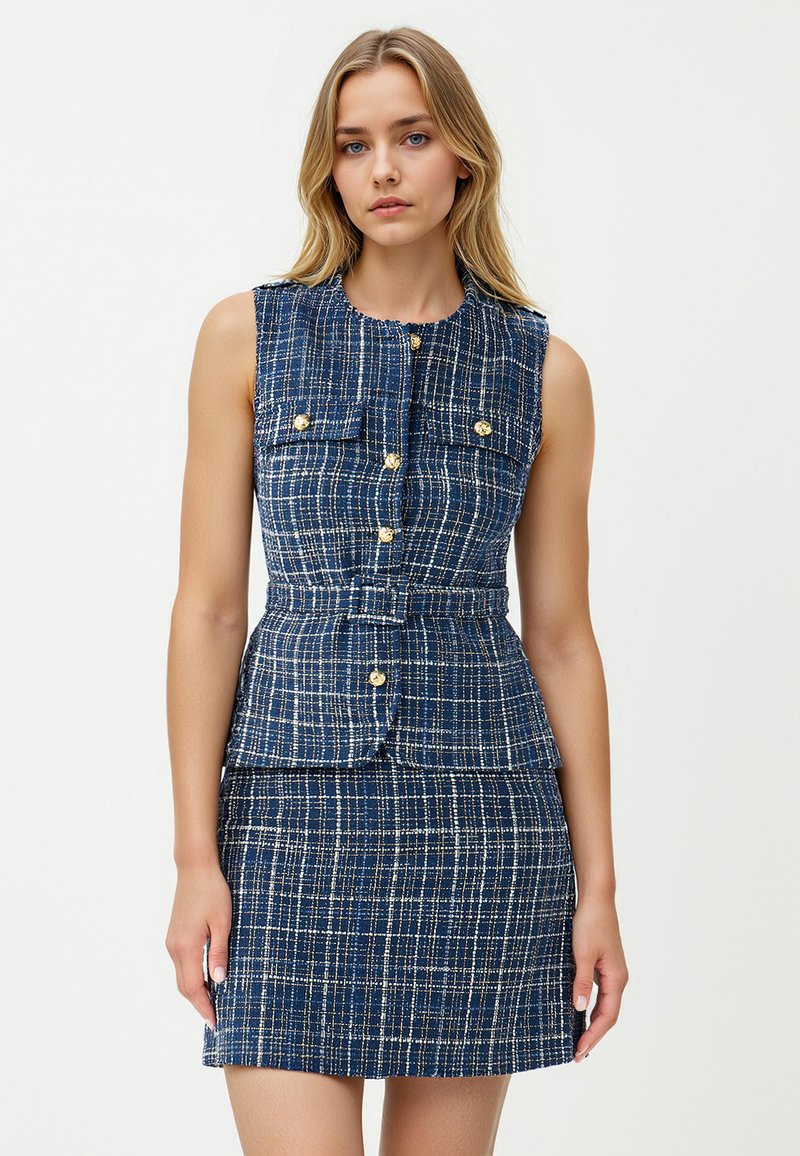 Abito senza maniche blu navy con un motivo a quadri testurizzato, caratterizzato da bottoni dorati e un accentuato punto vita a peplo. Include due tasche sul petto.