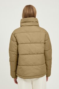 Giacca puffer kaki con colletto alto, caratterizzata da sezioni trapuntate e una texture morbida, cuciture visibili e una vestibilità rilassata.