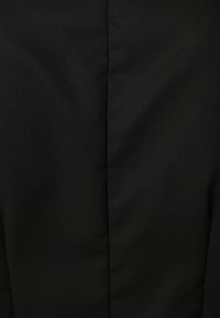 Gros plan sur un tissu noir lisse avec une couture centrale et une texture subtile, probablement partie d'un vêtement.