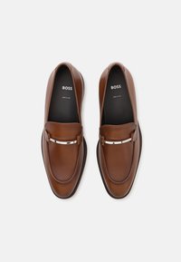 Mocassins en cuir marron au design élégant, avec une garniture en métal argenté sur le cou-de-pied et un bout arrondi ; fabriqués en Italie. Marque BOSS visible à l'intérieur.