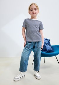 Koszulka w paski z krótkim rękawem, niebiesko-biała, w zestawie z luźnymi niebieskimi jeansami. Buty sportowe są białe z czarnymi akcentami.