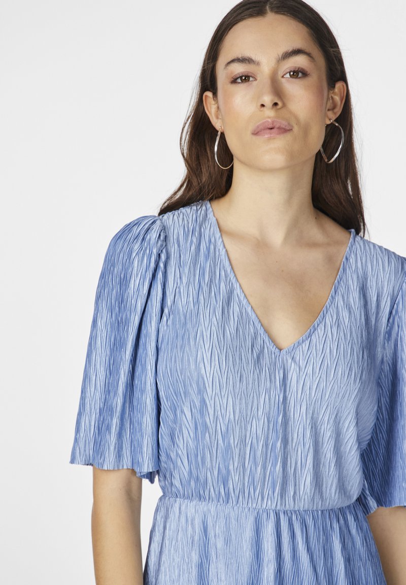 Jasnoniebieska sukienka z teksturowanej tkaniny, z pionowymi wzorami w zygzak, dekoltem w kształcie litery V oraz krótko puffowanymi rękawami.