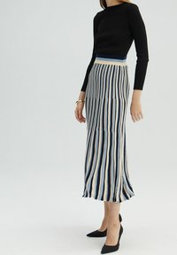 Top long-sleeve ajusté noir associé à une jupe mi-longue rayée avec des rayures verticales bleues, crème et marine, complétée par des talons aiguilles noirs.