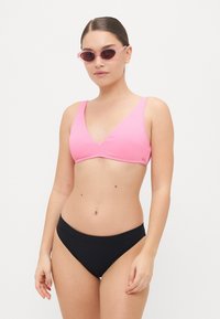 Rózsaszín bordázott bikini felső mély V nyakkivágással, amelyet sima fekete bikini alsóval párosítanak. Széles pántokkal és sima szövettextúrával rendelkezik.