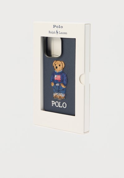 Θήκη τηλεφώνου από δέρμα σε ναυτικό μπλε με κεντητό αρκουδάκι Polo που φοράει πουλόβερ, τζιν, μπότες και τη λέξη "POLO" από κάτω, σε λευκή συσκευασία.