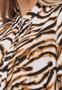 Koszula z kołnierzykiem w abstrakcyjny wzór tygrysich pasków w kolorach czarnym, pomarańczowym i białym, wykonana z lekkiej, teksturowanej tkaniny.