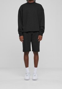 Svart sweatshirt med hög krage och sänkta axlar, matchad med svarta shorts. Vita sneakers med snörningar och ankelsockor.