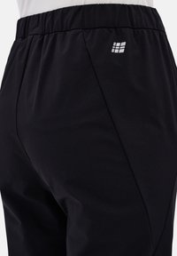 Schwarze Jogginghosen mit elastischem Bund, ausgestattet mit einem kleinen weißen Logo an der Seite und einem glatten, leichten Stoff.