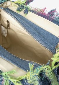 Interno di una borsa in tessuto frangiato multicolore, con fodera in denim, una tasca con zip e materiale in tela beige.