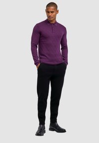 Paarse longsleeve polo met een texturaal ruitpatroon, gecombineerd met zwarte tapered pants en zwarte enkellaarsjes.
