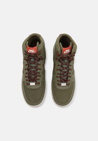 Green high-top sneakers with leather and textile upper, orange laces, padded collar, and perforated toe box. Nike logo on tongue and side.