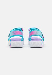 Colorful sandals with turquoise and pink straps, adjustable closures, and a white sole featuring a textured pattern on the bottom.
