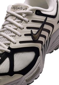 Valkoiset ja mustat urheilukengät, joissa on verkkokangaspinta, metalliset yksityiskohdat, tekstuuriset päällysteet ja pehmustettu pohja, jossa on brändäys sivulla.