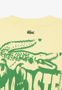 Geel katoenen T-shirt met een grote groene krokodilafbeelding en een geborduurd groen krokodillogo bij de hals.