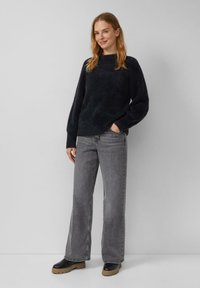 Ciemnoszary, wełniany sweter z wysokim kołnierzem i szerokimi rękawami, w zestawie z jasnoszarymi, szerokimi spodniami i czarnymi botkami na platformie.