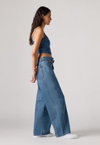 Top cropped de ganga e calças largas em azul claro. O tecido tem uma textura clássica com costuras visíveis e detalhes subtis nos bolsos.