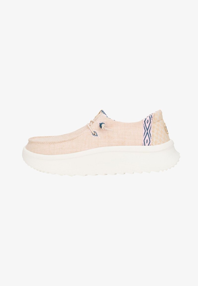 Zapato casual beige tipo slip-on con suela blanca gruesa, cordones de tela y detalles estampados en azul y blanco en el talón y el cuello.