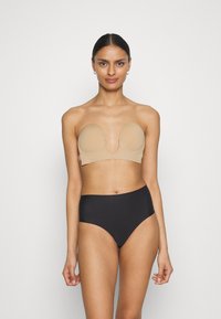 Soutien-gorge nude sans bretelles avec bonnets moulés, tissu lisse et décolleté arrondi, associé à un pantalon noir taille haute. Design simple, sans matériel visible.