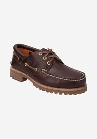 Brauner Lederbootsschuh mit weißer Naht, runder Zehenpartie, goldenen Ösen und einer robusten Gummisohle. Besitzt ein Logo an der Seite.