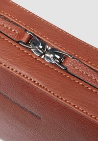 Primo piano della cerniera di una borsa in pelle marrone con due tiretti in metallo argento e cuciture dettagliate sulla superficie liscia della pelle.