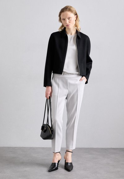 Giacca cropped nera, blusa bianca, pantaloni grigi chiari su misura, mules neri e una piccola borsa a mano. Tessuti lisci e design strutturato.