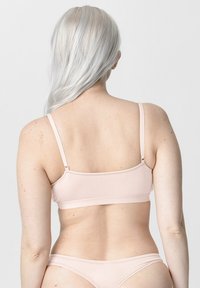 Lichtroze beha van een gladde, rekbare stof, met brede verstelbare bandjes en een minimalistisch ontwerp. Voorzien van een haak- en oogsluiting aan de achterkant.